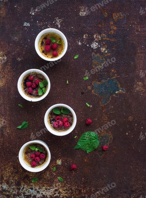 Preview: Creme brulees with raspberries and mint in white bowls over grunge metal backdrop. Top view