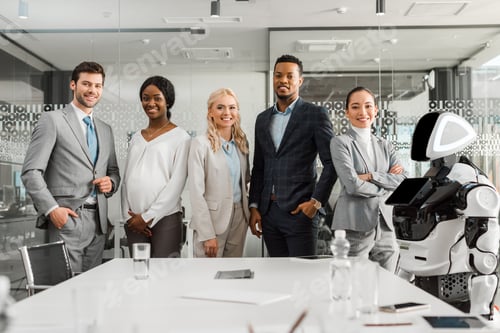 Preview: smiling multicultural businesspeople looking at camera while standing near robot in conference hall