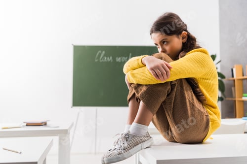 Preview: upset and bullied schoolgirl sitting alone in classroom