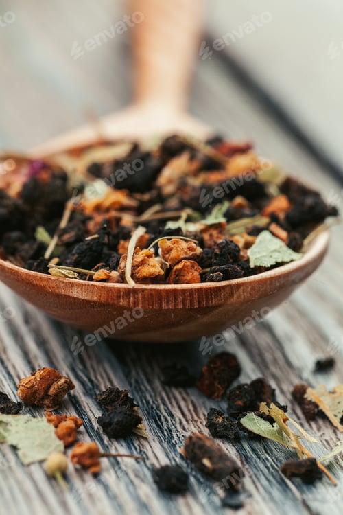 Preview: Black tea with herbs in wooden spoons on a wooden board