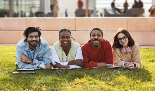 Preview: Happy young multiethnic people students lie on green grass, rest at free time, study with device