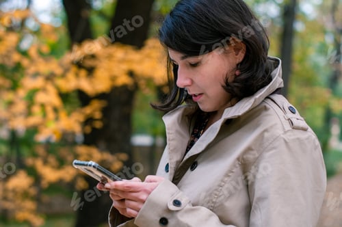 Preview: Young woman holding her phone, autumn background