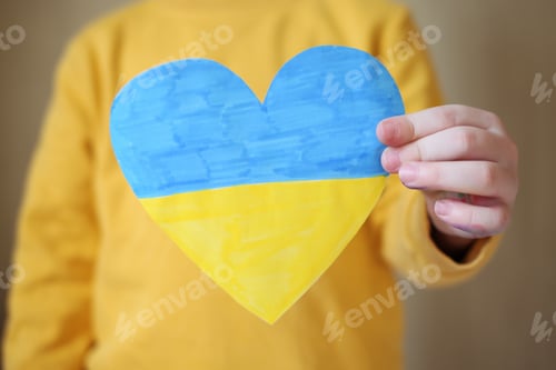 Preview: A small refugee boy from Ukraine with a drawing of the Ukrainian flag.