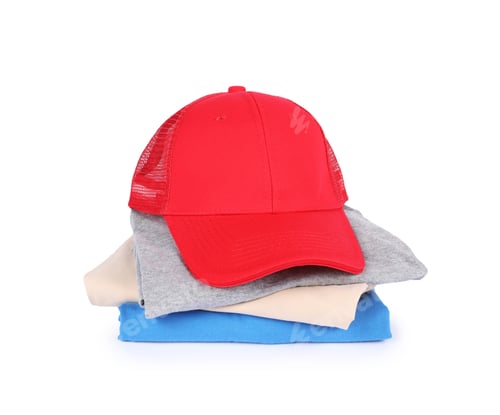 Preview: Red baseball cap and stack of folded t-shirts isolated on white. Mockup for design