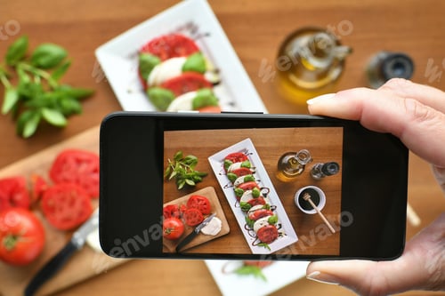 Preview: Social media influencer taking photo with smartphone of food, Caprese salad, to post online.