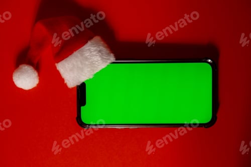 Preview: Mobile phone dressed in Santa-Claus red-white hat with chroma key screen against red background