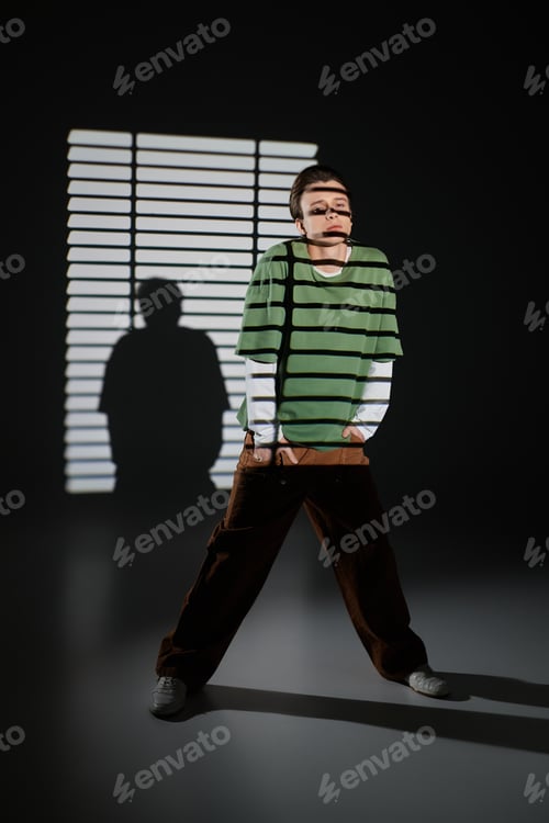 Preview: Stylish teenage boy stands confidently in shadowy light at a creative studio