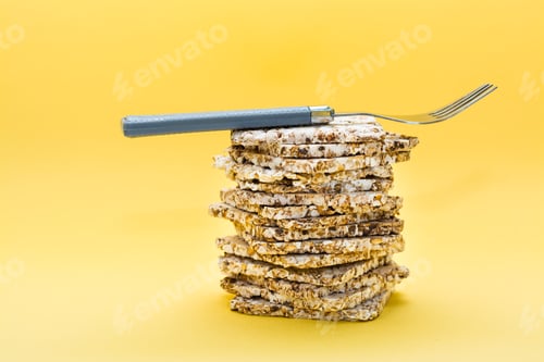 Preview: Crispbread made from oats, wheat, flax and sesame seeds in a stack and a fork on it on a yellow
