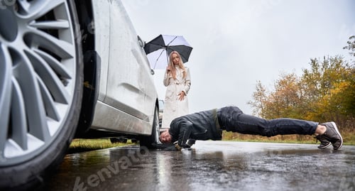 Preview: Charming young woman watching how man fixing car wheel.