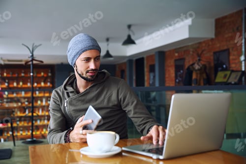 Preview: Young handsome hipster man with beard is using computer in cafeteria