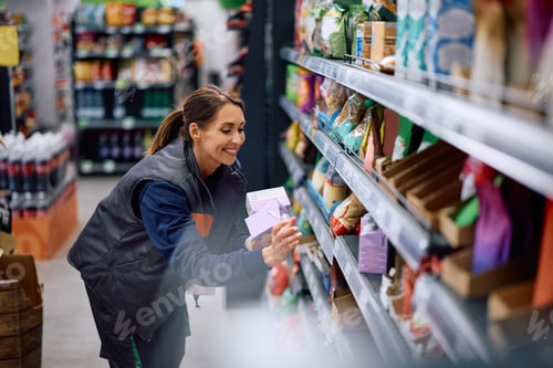 Preview: Happy female worker sorting products on shelves in supermarket.
