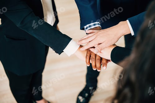 Preview: Colleagues from various ethnicities and backgrounds join hands in a modern office, emphasizing