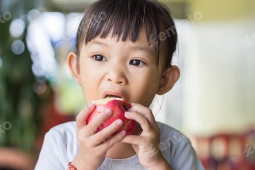 Preview: Happy Asian child girl eating and biting an red apple. Enjoy eating moment. Healthy food