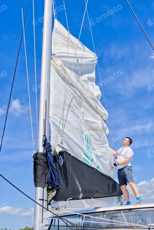 Preview: Raising the sail on a yacht. Young man captan lifting the sail of catamaran yacht during cruising