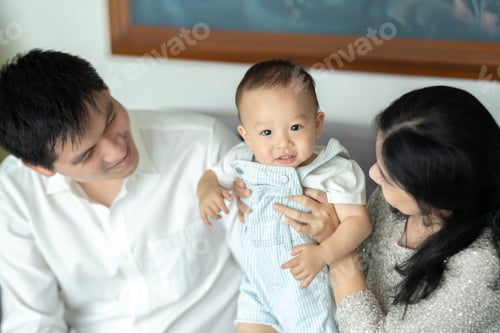 Preview: Young cheerful mother and father sitting on couch relaxing play with cute little new born baby boy