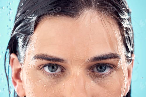 Preview: Water splash, skincare and eyes of woman in shower in studio isolated on a blue background. Beauty,