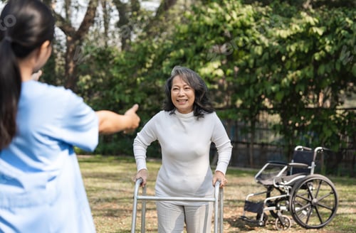 Vorschau: Ältere Frau mit Pflegekraft bei Rehabilitationssitzung im Freien mit Gehhilfe und Rollstuhl