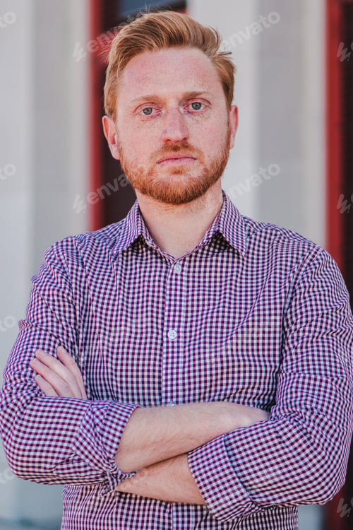 Preview: Vertical individual portrait of arms crossed serious young adult man standing outdoors and looking