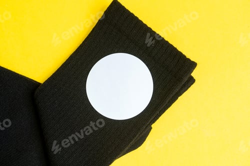 Preview: Black socks with a round sticker on a yellow table