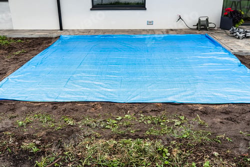 Preview: Rolling yellow sand with a steel roller for a garden pool, visible blue tarpaulin.