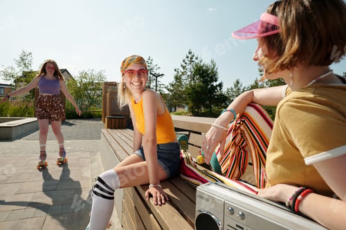 Preview: Happy young female roller skater looking at one of her friends at break