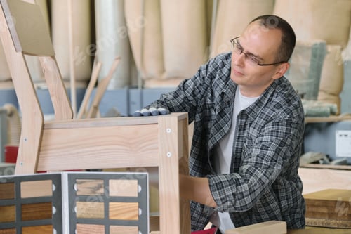 Preview: Male carpenter working in furniture joinery, master making wooden chair in wood workshop