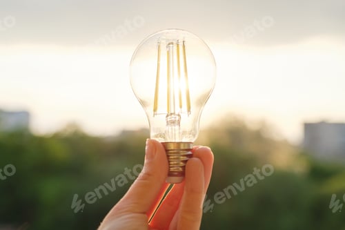 Preview: Filament led lightbulbs, hand holding lamp, evening sunset sky background