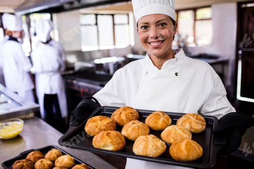 Preview: Female chefs holding baking tray of kaiser rolls in kitchen