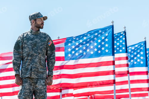 Preview: soldier in uniform standing near american flags against blue sky