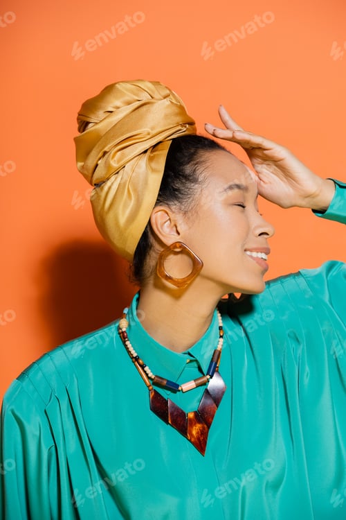 Preview: Side view of smiling african american woman in blouse and headband on orange background