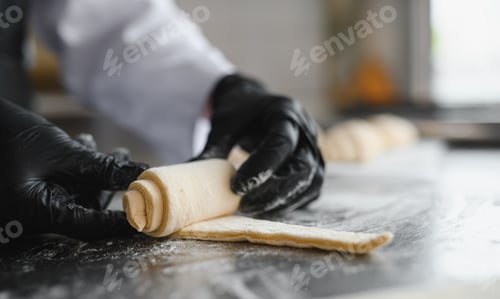 Preview: Baker rolling dough for croissants in bakery kitchen