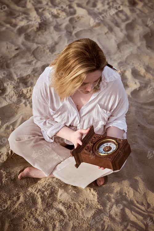 Preview: Reflective moment: young woman with clock on sandy beach
