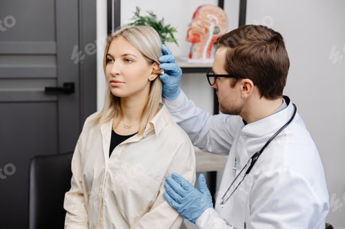 Preview: Otolaryngologist doctor checking young woman's ear using otoscope or auriscope at ENT clinic