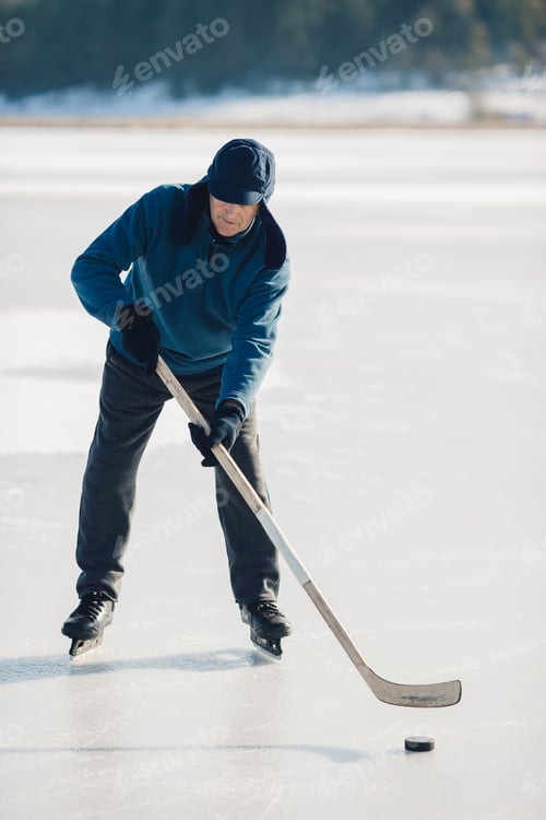 Preview: An elderly man practices stricking the puck with hockey sticks on a frozen lake in winter.