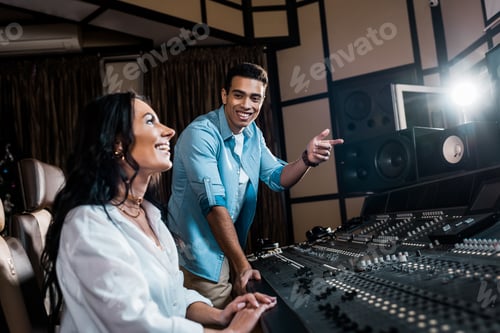 Preview: smiling handsome sound producer pointing with finger near pretty smiling colleague