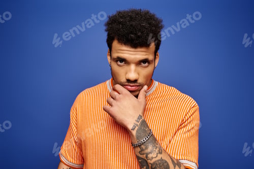 Preview: Handsome man in vibrant orange shirt poses confidently against a blue background