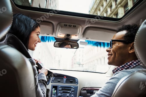 Preview: A young woman and young man in a car looking at each other and smiling, seen from the back seat.