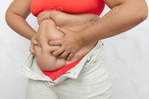 Preview: Hands of overweight woman with effort compress hanging folds on belly closeup, white background