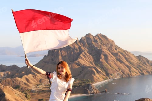 Preview: A woman on top of hills holding indonesian flag celebrating independence day