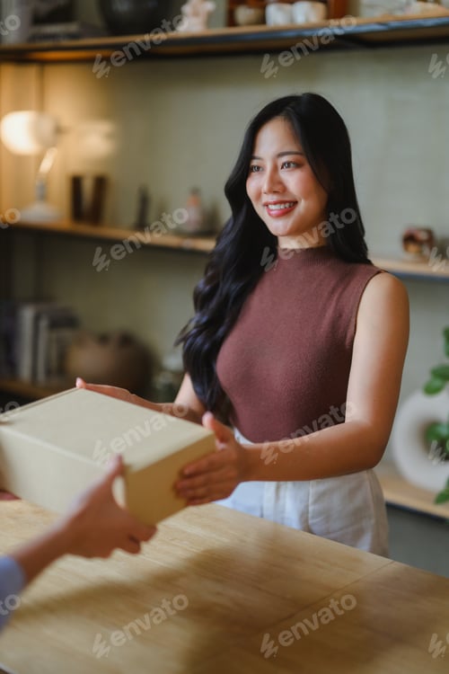 Preview: Smiling young shop assistant receiving parcel from delivery man in her store