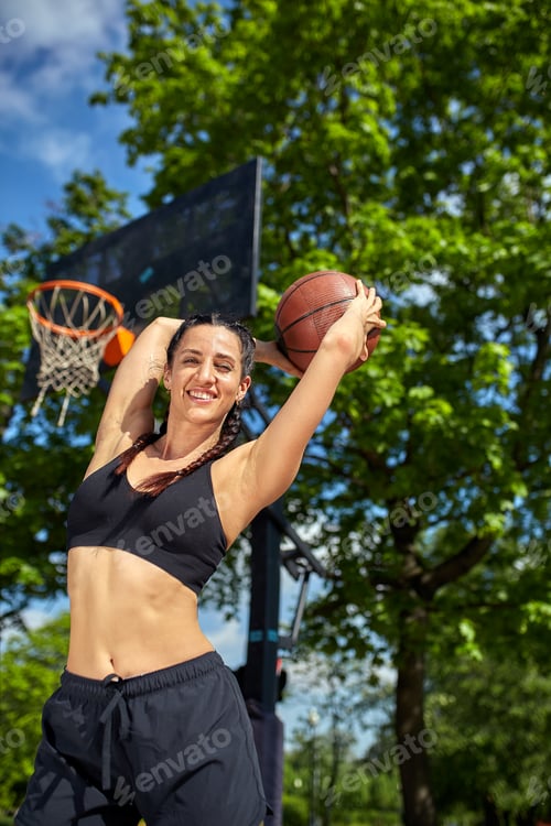 Preview: Beautiful, sporty latin girl with a basketball under the ring on a street basketball court. Sport
