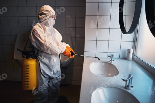 Preview: Professional female cleaner in a hazmat suit disinfecting surfaces