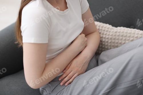 Preview: Young woman suffering from stomachache at home, closeup