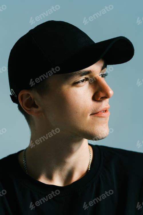 Preview: Portrait of stylish handsome caucasian man fashion model in t shirt and cap, studio shot.