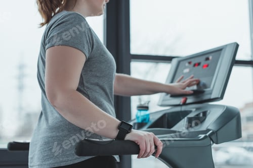 Preview: Curvy girl adjusting treadmill in gym