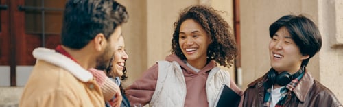 Preview: Happy students talking each other standing near university campus and holding books and laptop