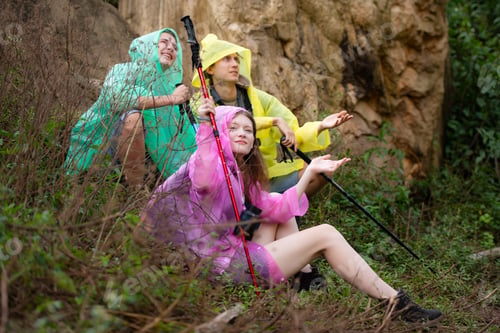 Preview: Group of friends in raincoat with backpacks hiking in the forest, Sit and shelter from the rain
