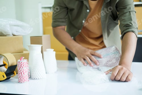 Preview: Young entrepreneur packing product in mailing box for shipping.