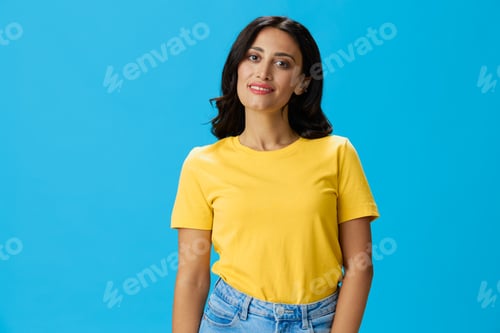 Preview: Woman in yellow t-shirt on blue background posing gestures emotions and signals with smile, hands up