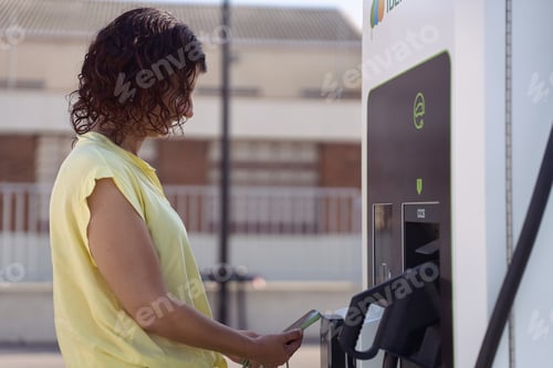 Preview: Woman paying for electric vehicle charging using smartphone at charging station